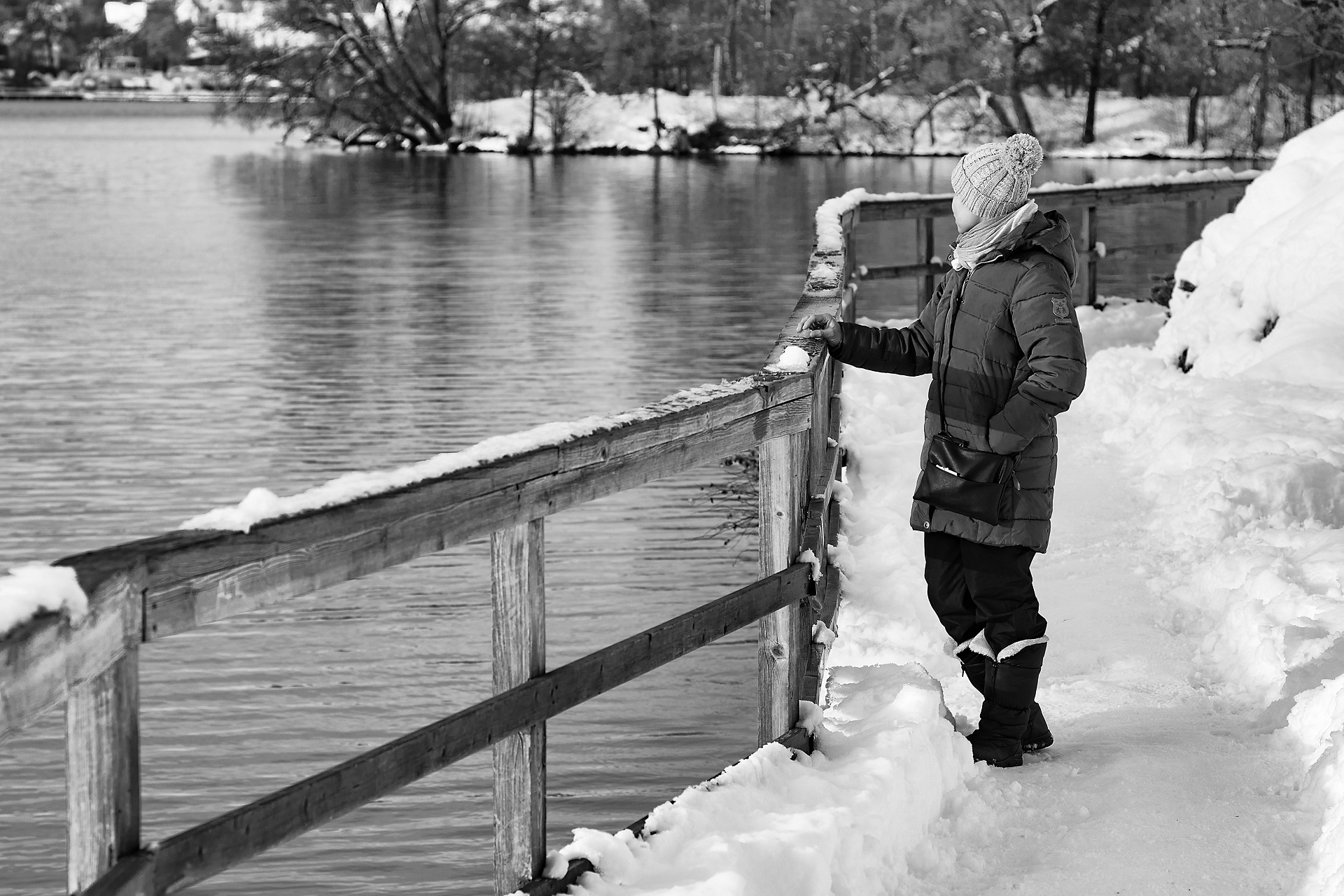 Person in a winter coat standing near a body of water with their hand on a fance.