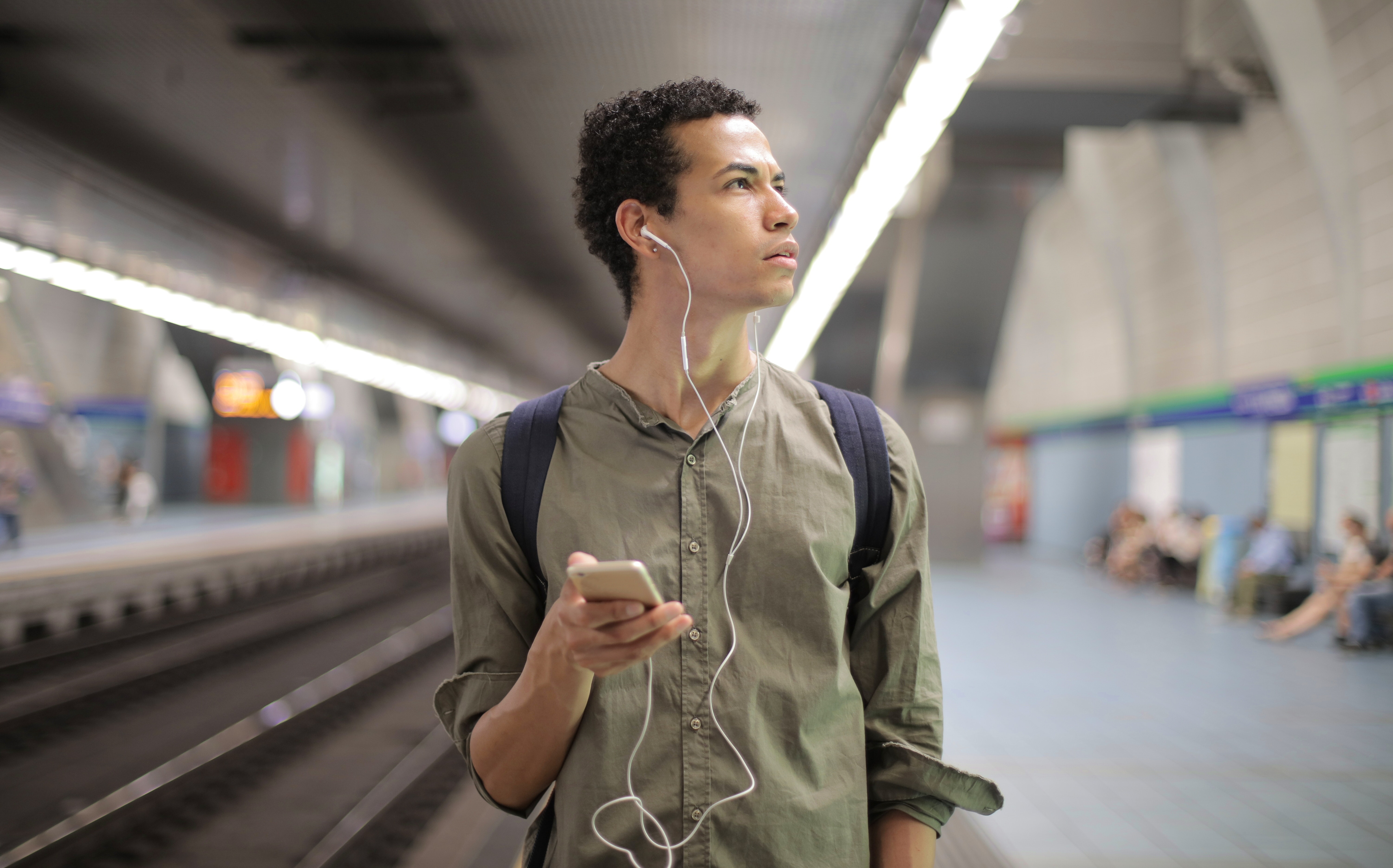 person wearing headphones while holding phone and looking to the side in a subway station