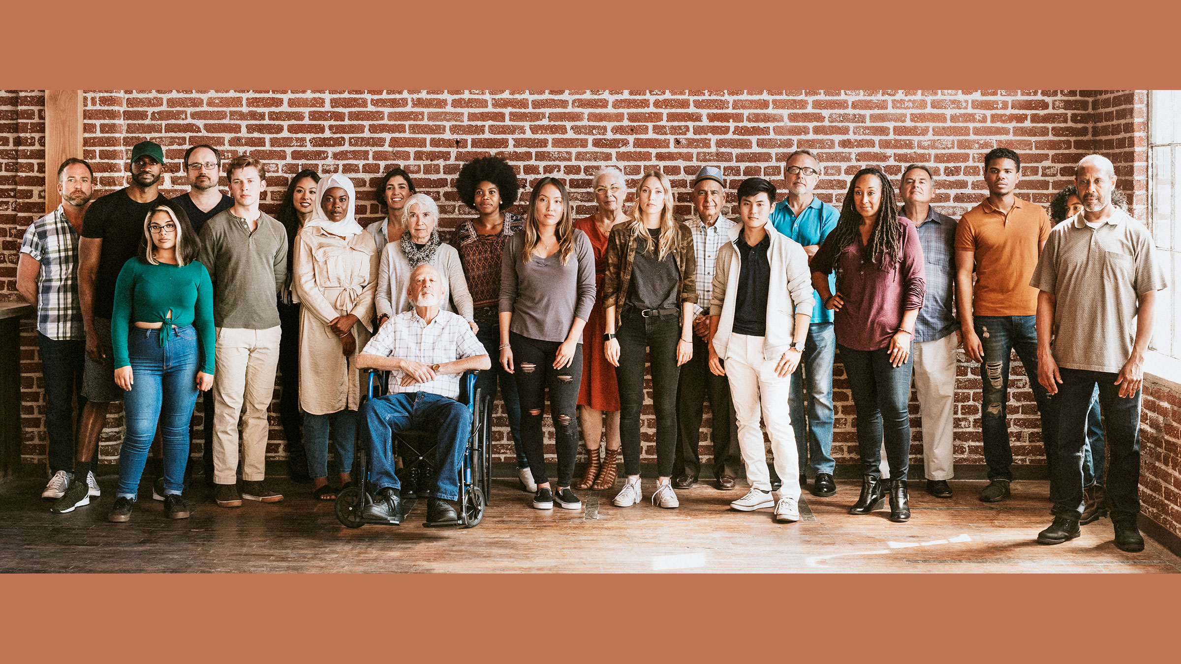 large group of people of all different genders, races, and abilities stand and sit in front of a brick wall