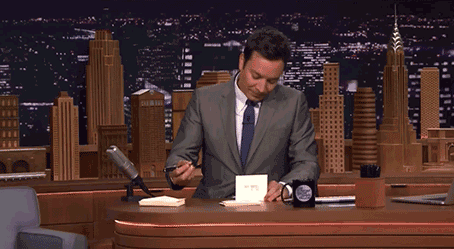 Jimmy Fallon sits behind his desk and writes on paper