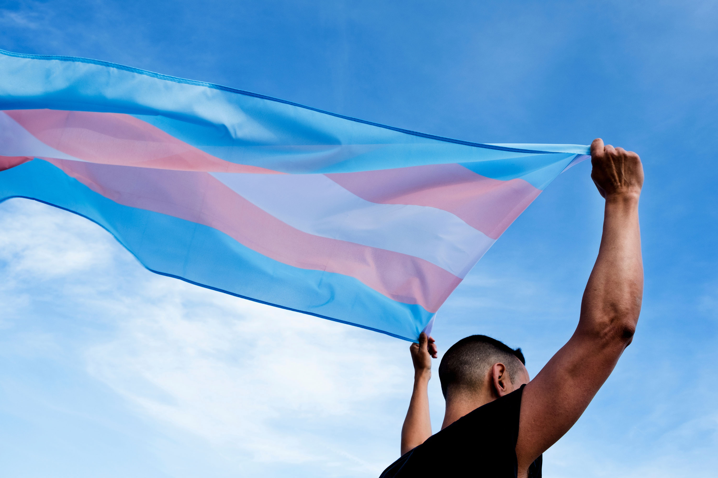 person holds up Transgender Pride flag which flies out behind them