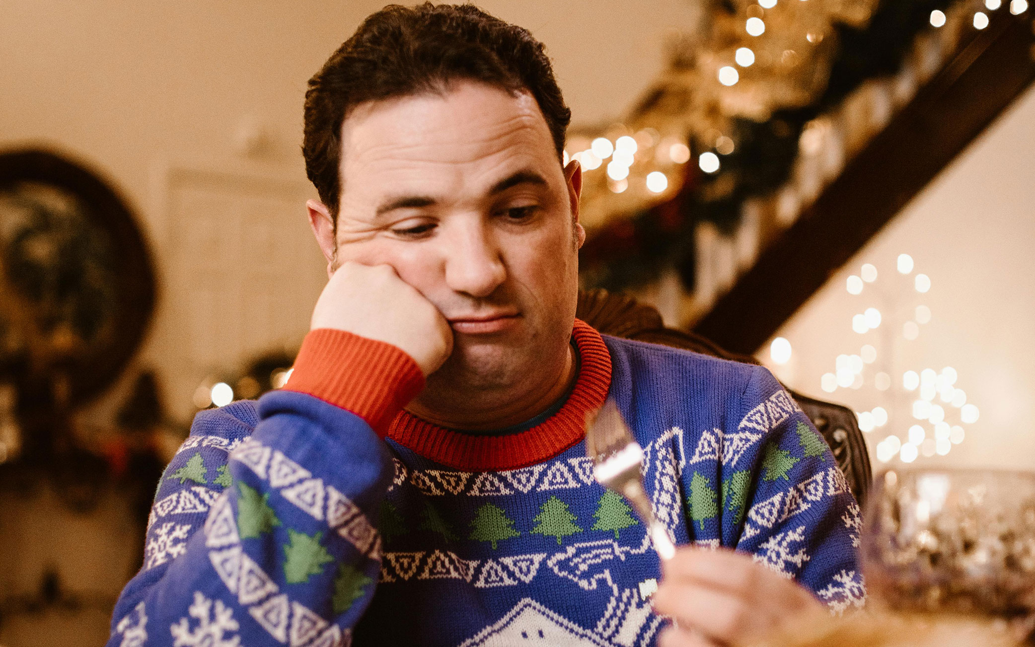 person in holiday sweater holds fork and looks at it dejectedly