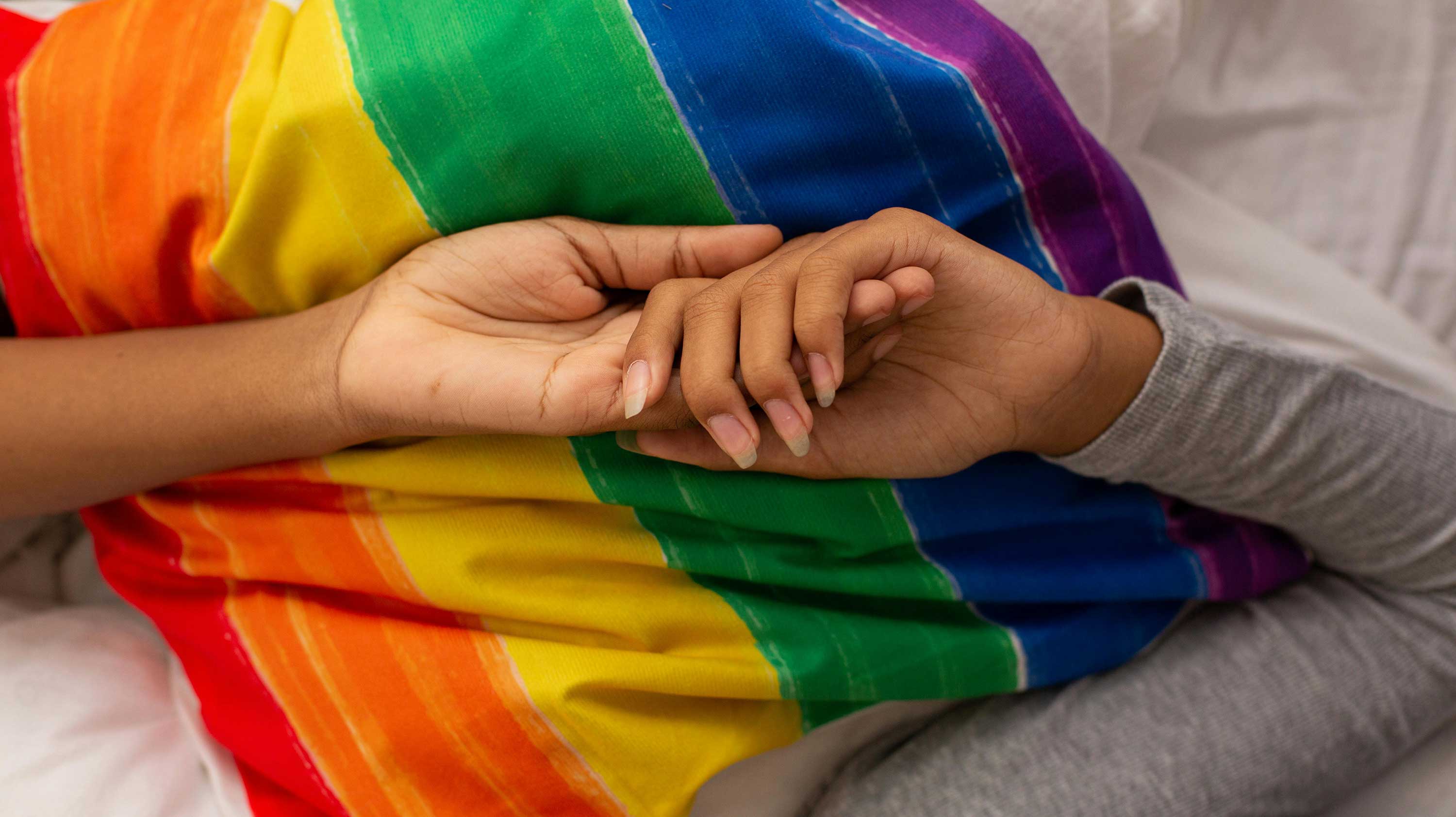two hands holding on top of rainbow pride flag