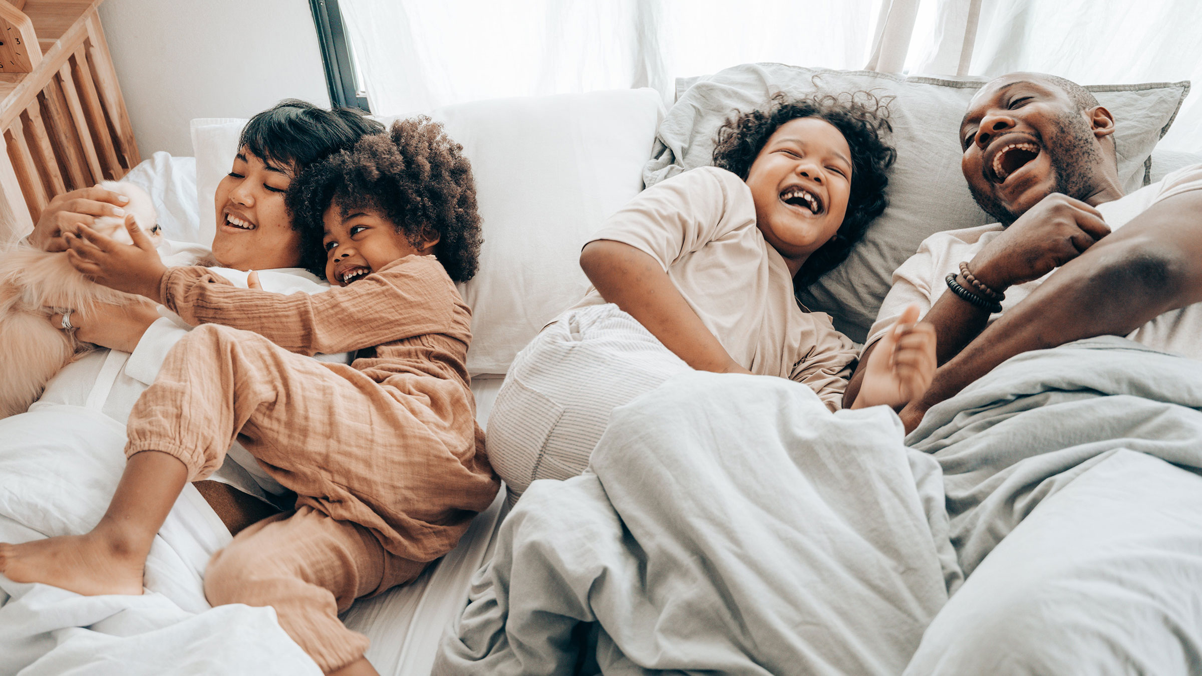 Multiracial family cuddles and laughs together on a bed