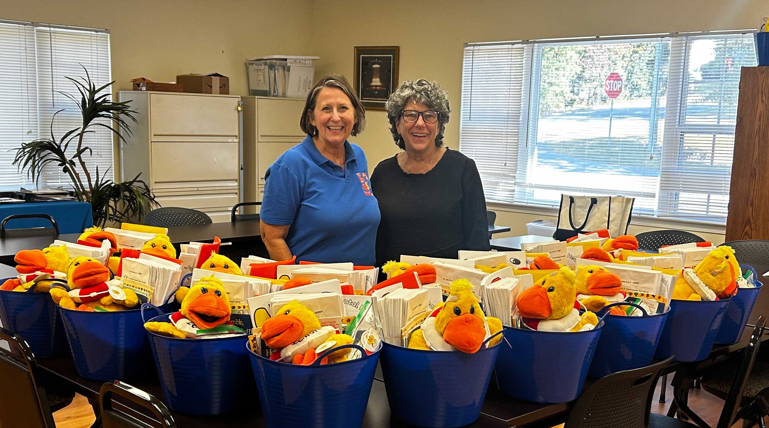 Volunteers stand with buckets of mental health resources on the tables in front of them.