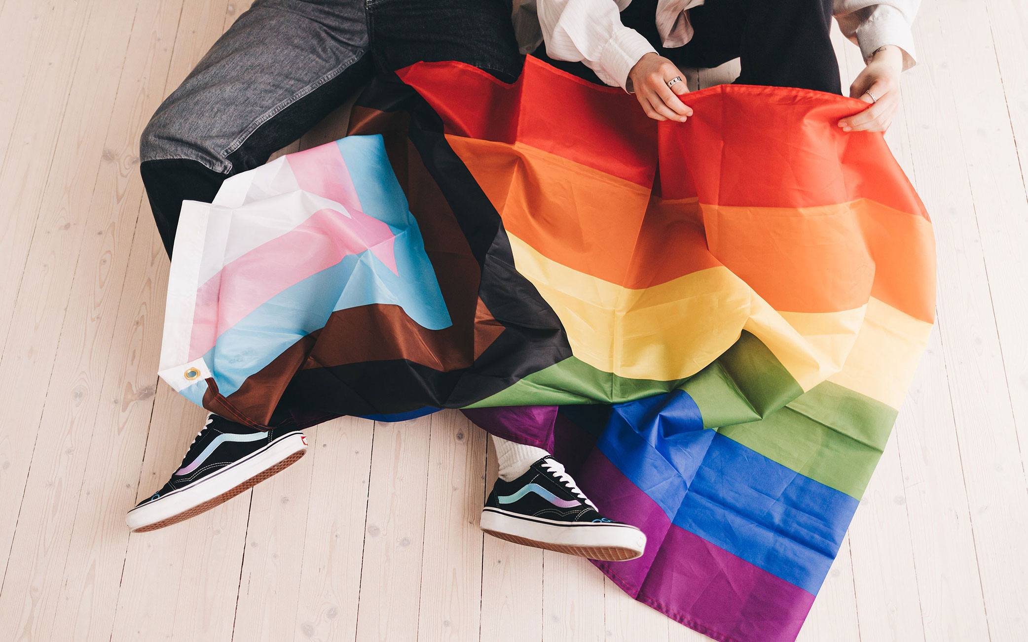 Progressive Pride flag laying over two pairs of legs