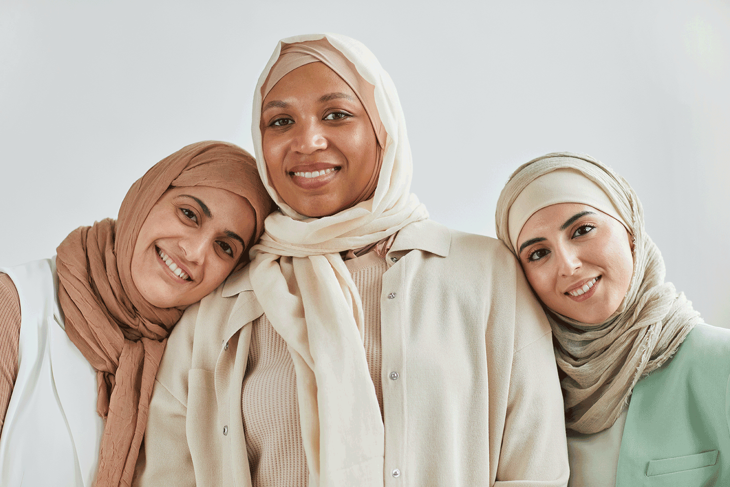 3 women stand next to each other wearing hijabs and smiling