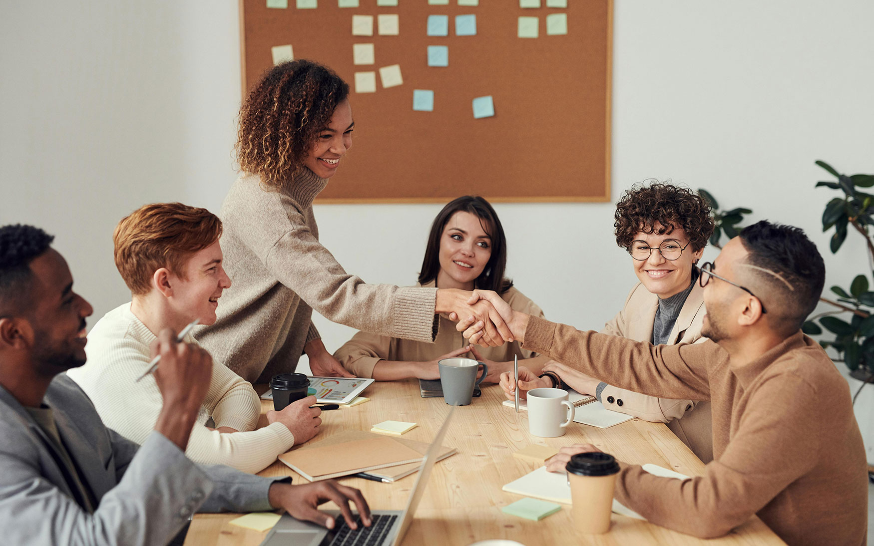 group of people sit around conference table while two of them shake hands