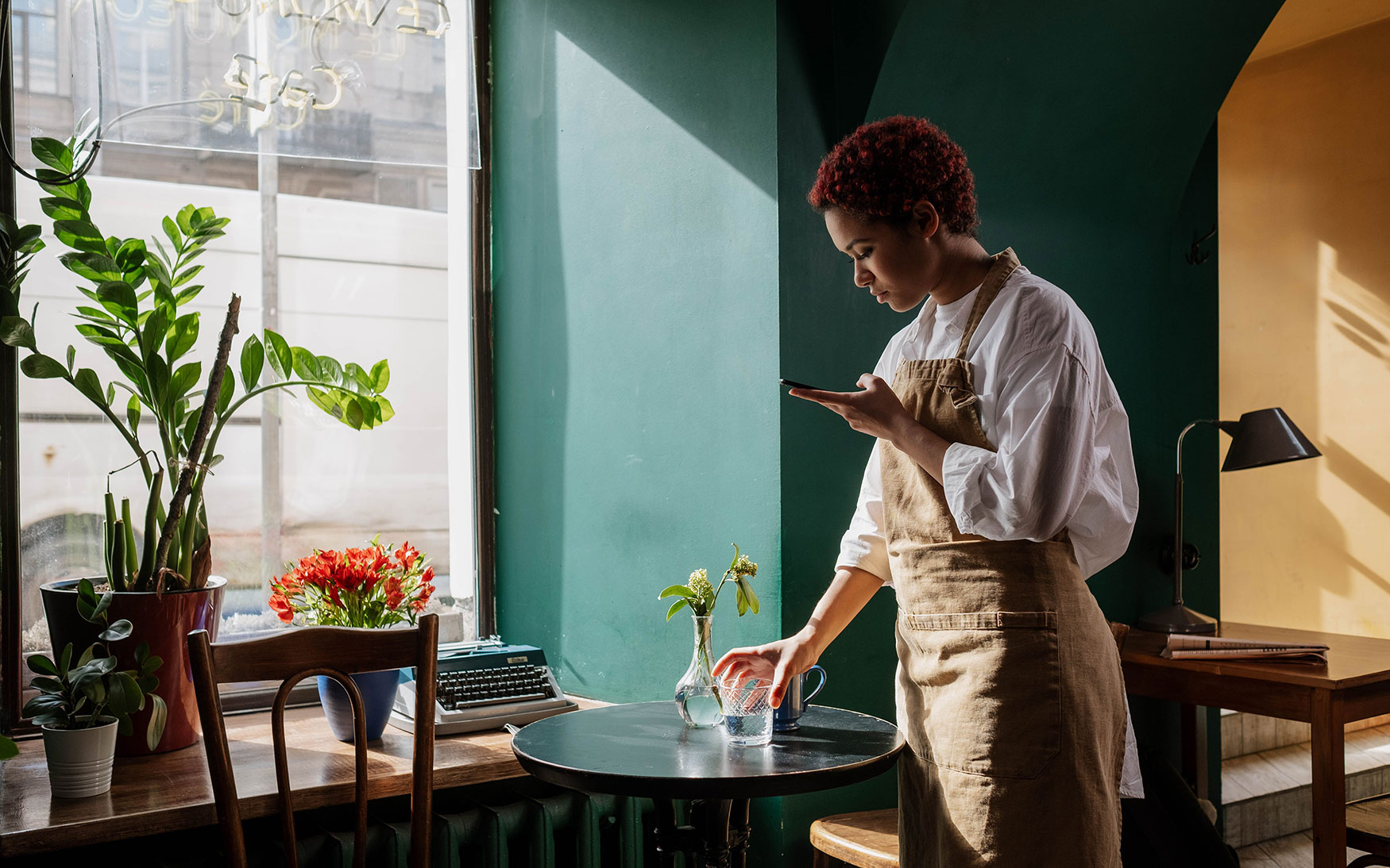 restaurant server in apron sets down glass of water while looking worriedly at phone