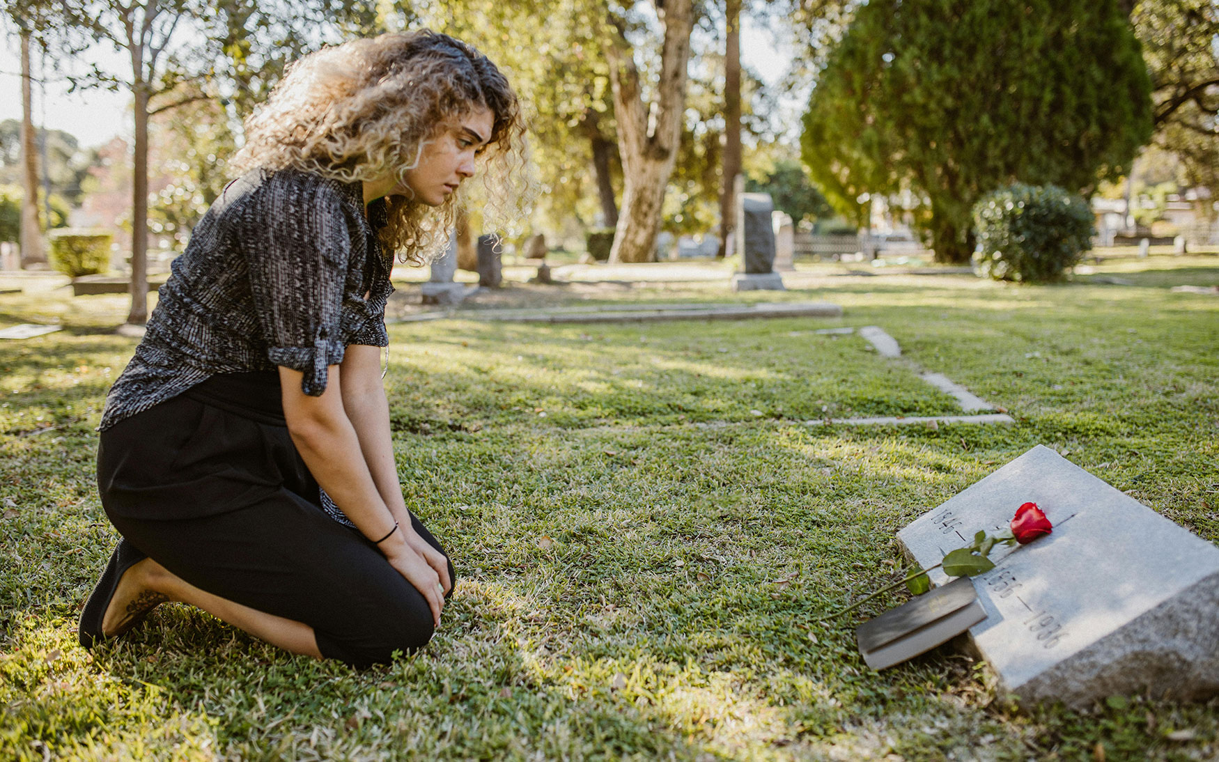 sad person sits in front of gravestone