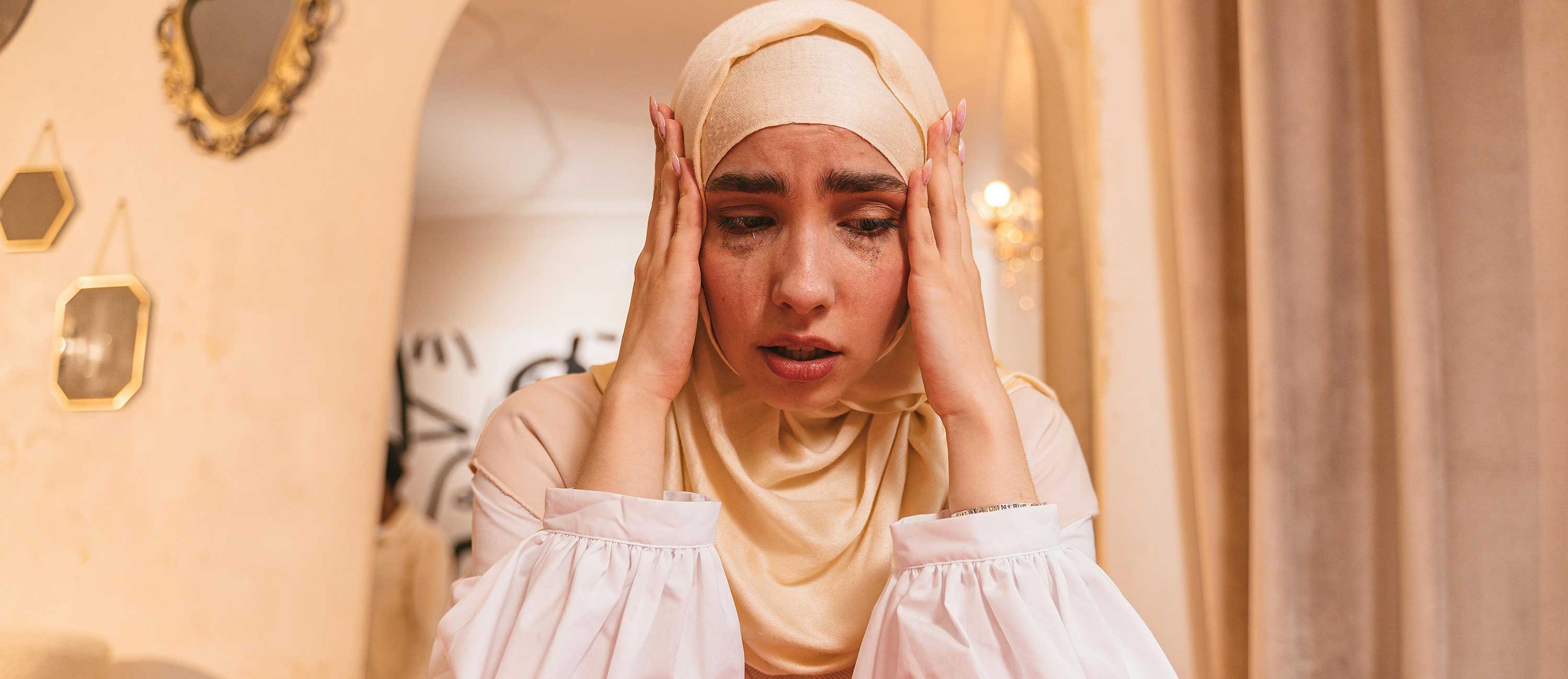 person wearing a hijab cries with head in hands