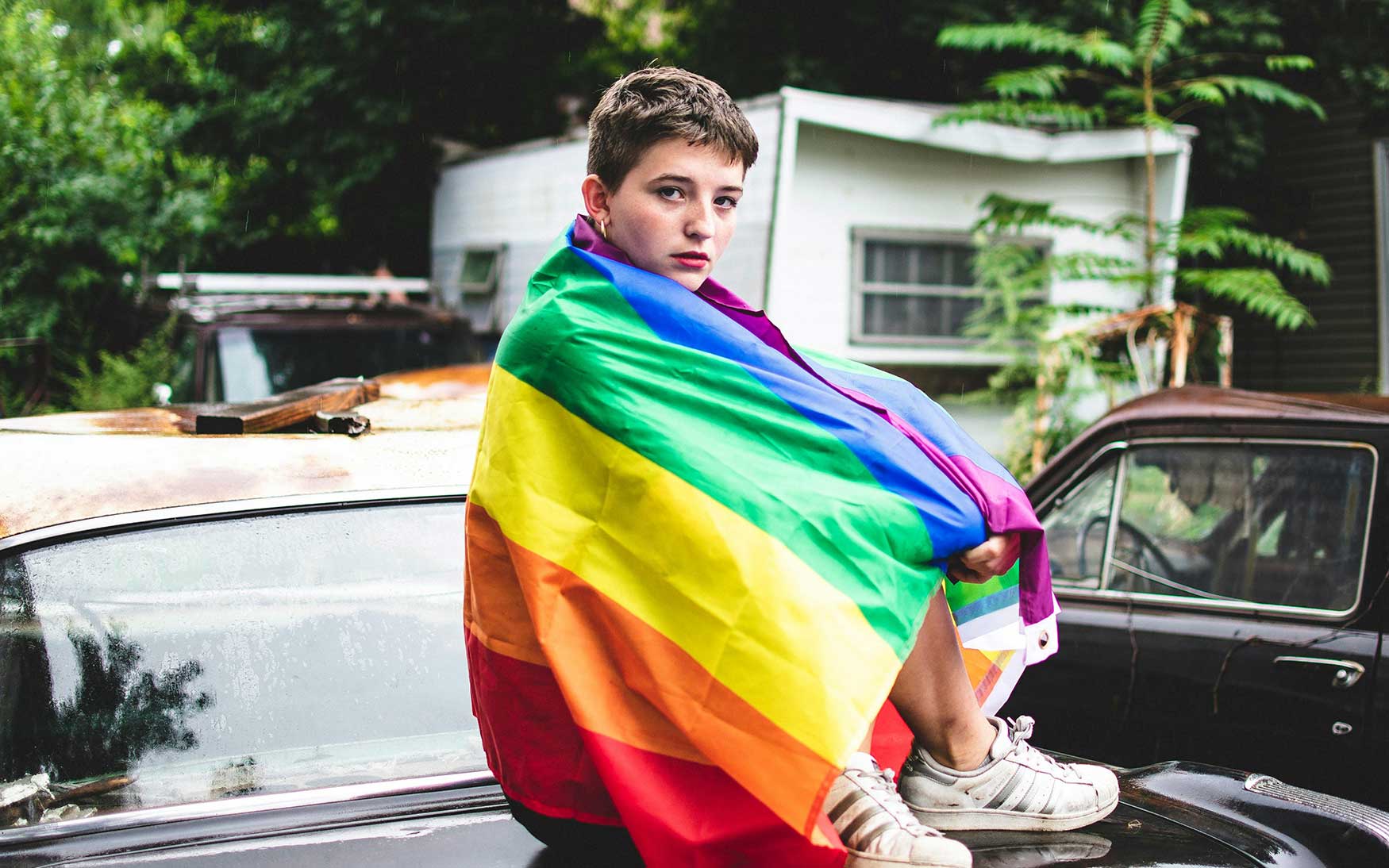 person sits with LGBTQ+ Pride flag wrapped around them