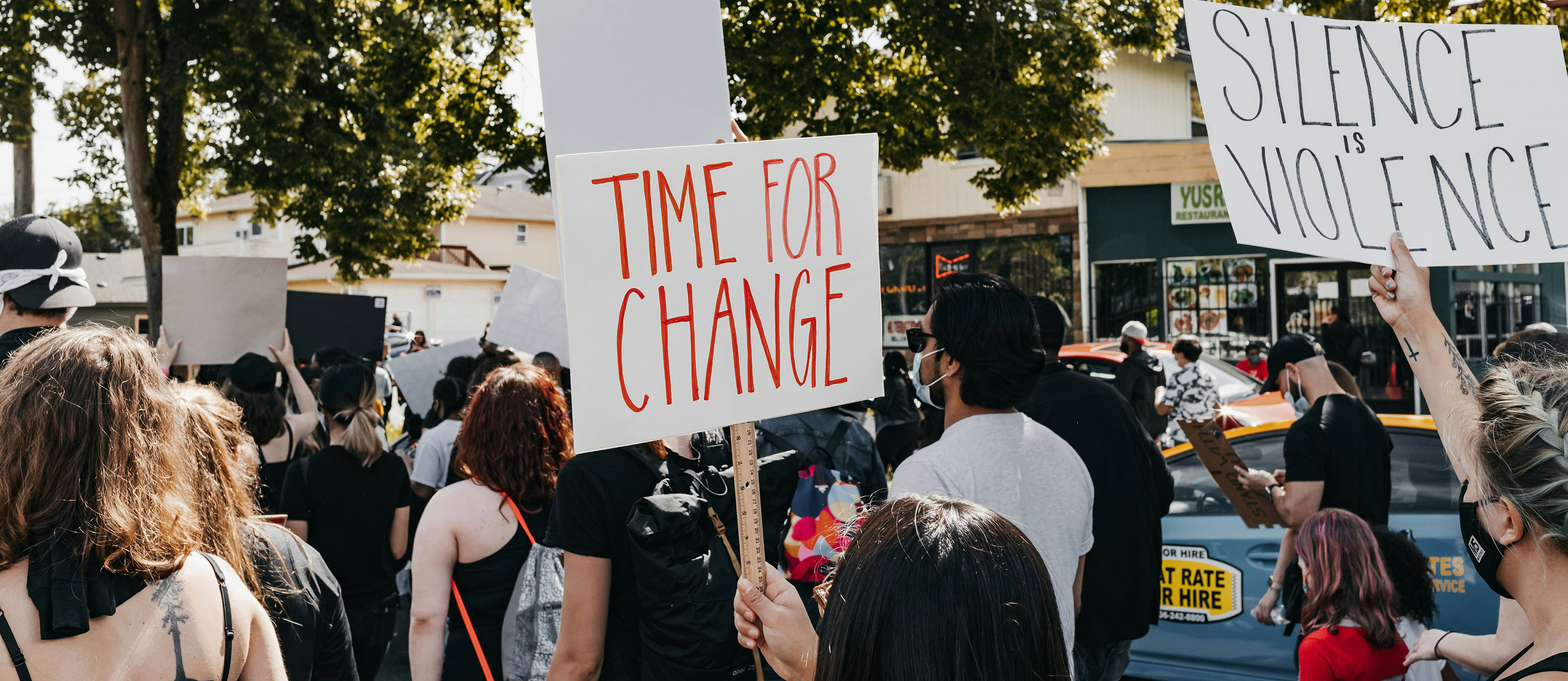 people participating in a march with signs saying Time for Change and Silence is Violence