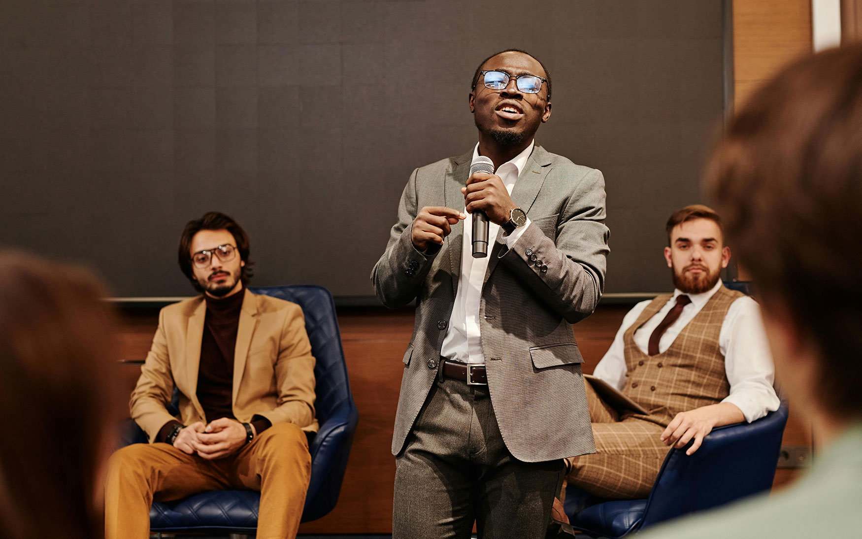 person stands and talks into microphone in among group of people