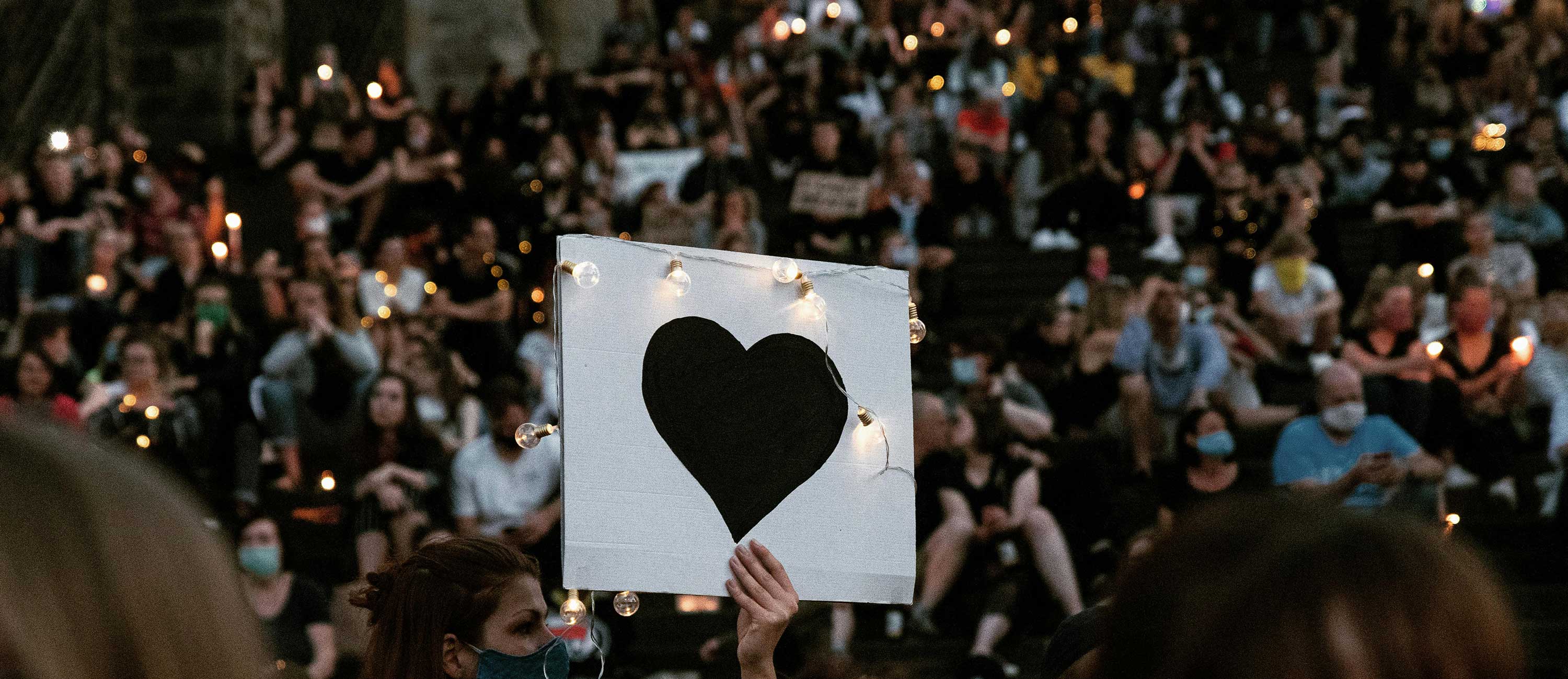 a candlelight vigil with one person holding up a white sign with a black heart