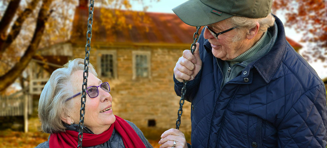 one elderly person sits on a swing while another person holds the chain of the swing