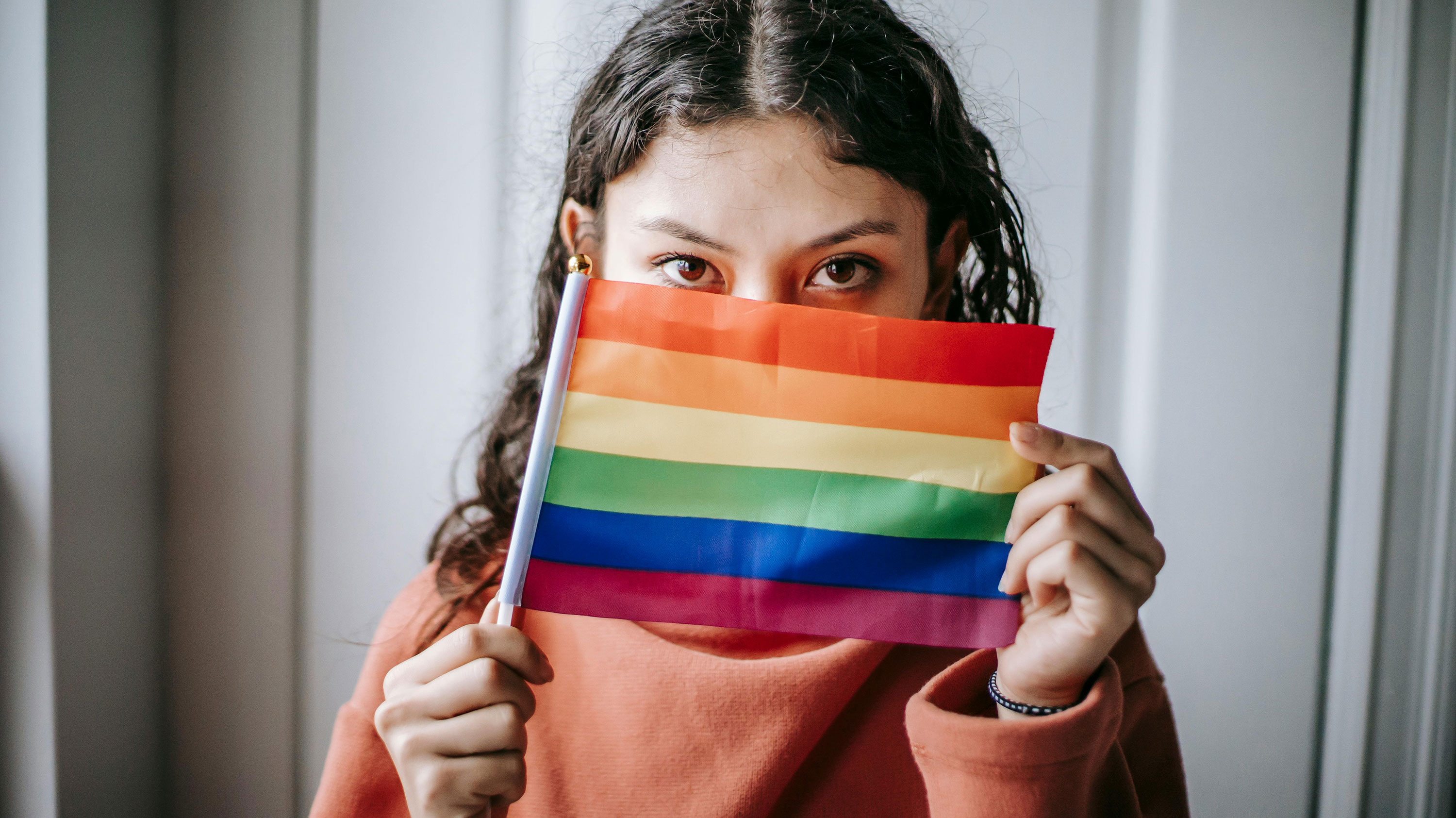 person holds rainbow pride flag up in front of their face