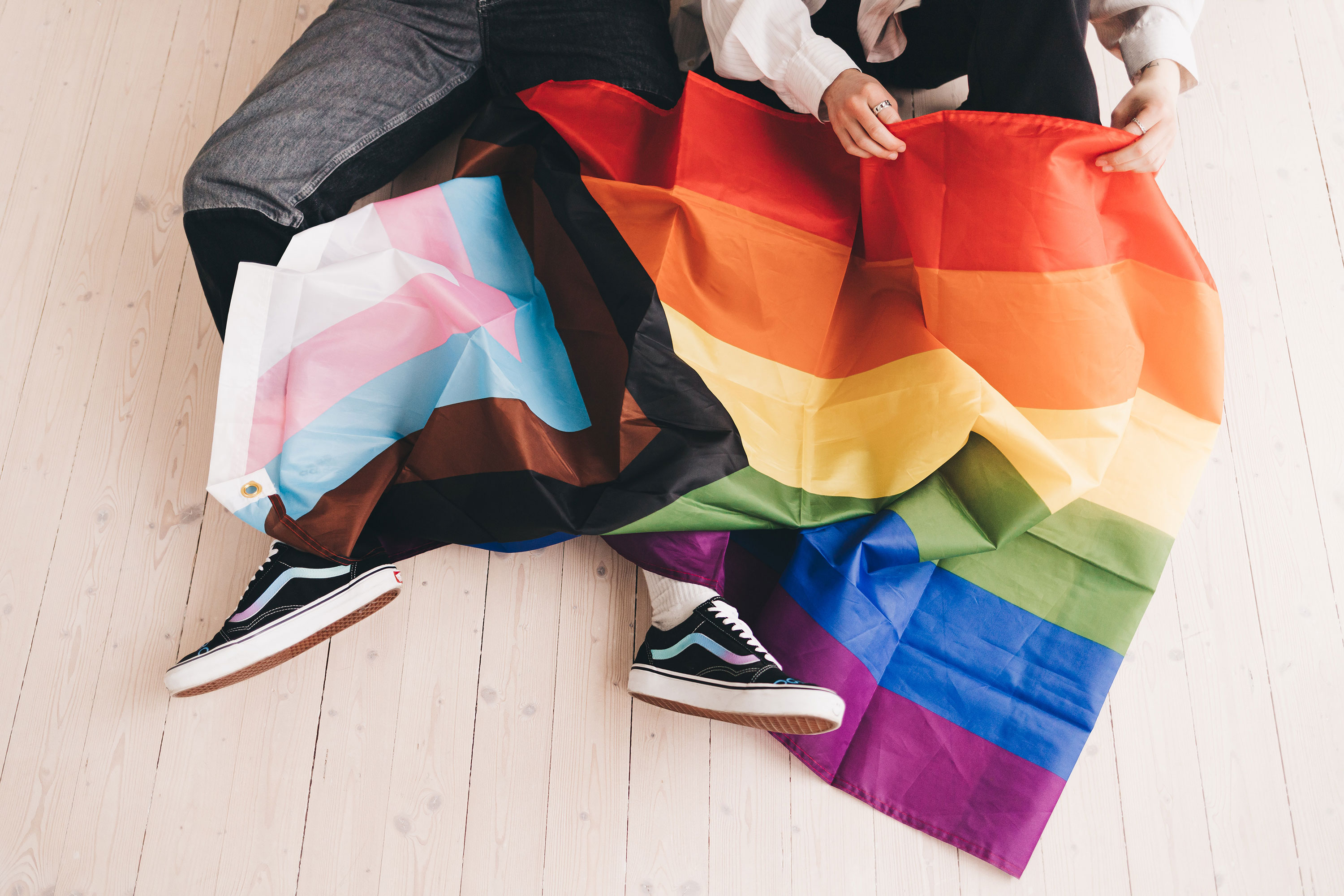 Progressive Pride flag lays over two pairs of legs
