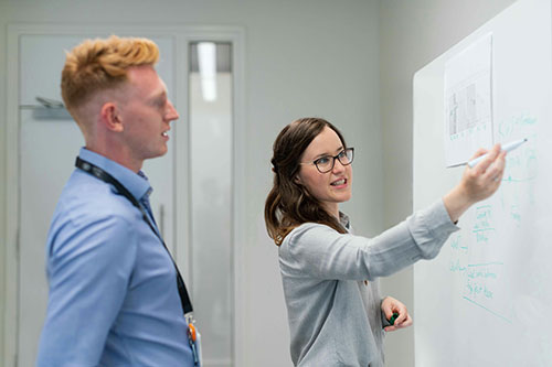 two people work together at a dry erase board