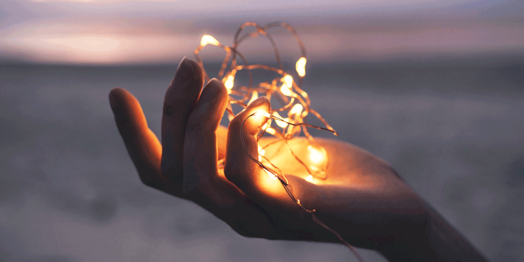 hand holds string of lights in front of a beach