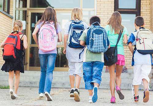 group of kids wearing backpacks walking into a school