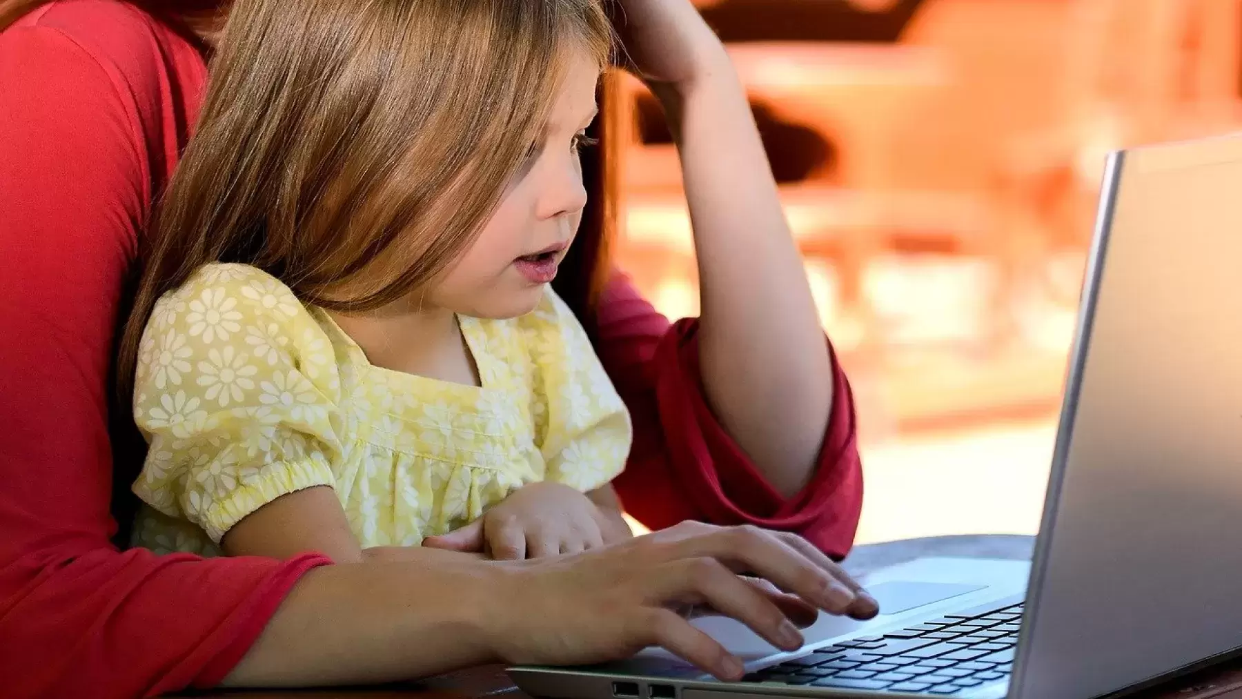 Young girl sitting in parents lap while they are on a laptop.