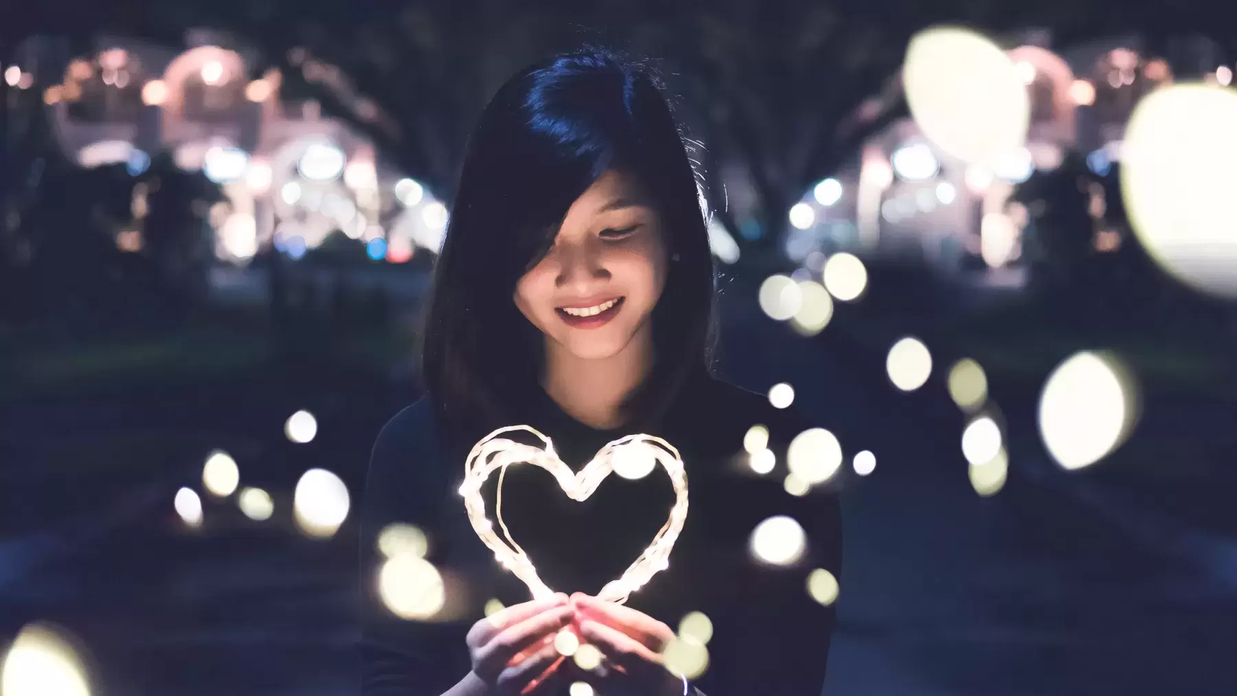 person holds lights shaped into a heart in their hands and smiles