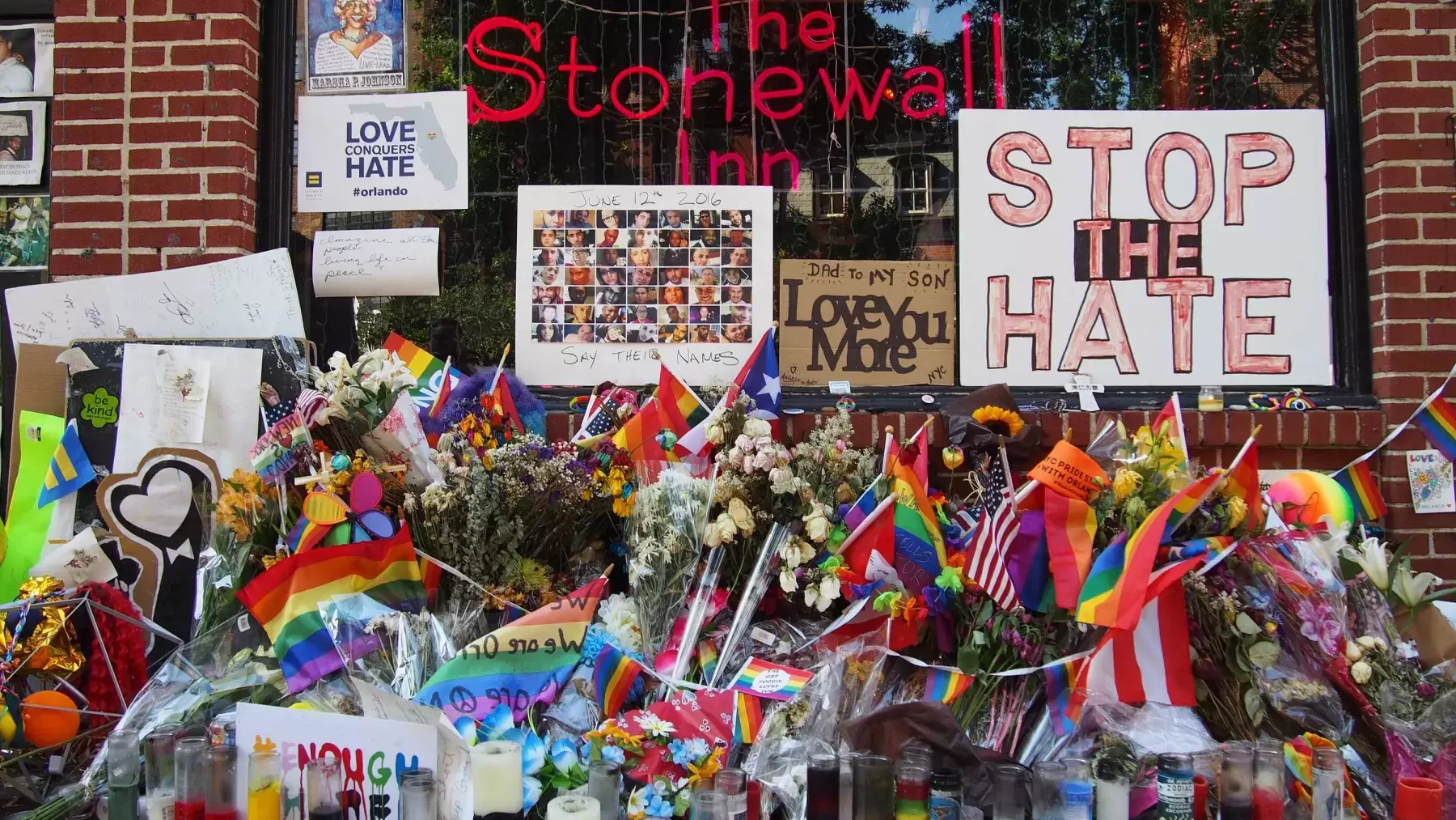 Flowers, flags, candles, and signs rest on the ground outside The Stonewall Inn