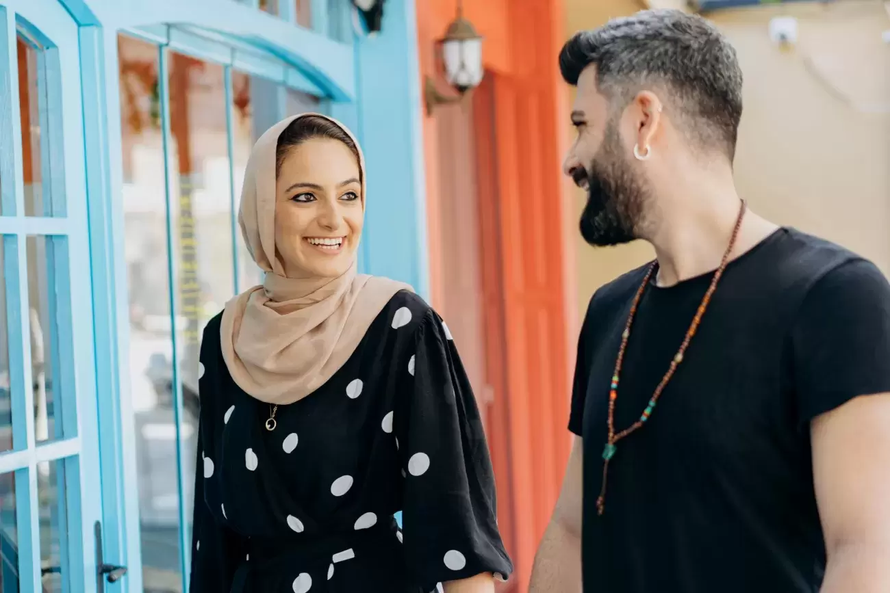 An Arab American couple walks side by side and smiles at each other