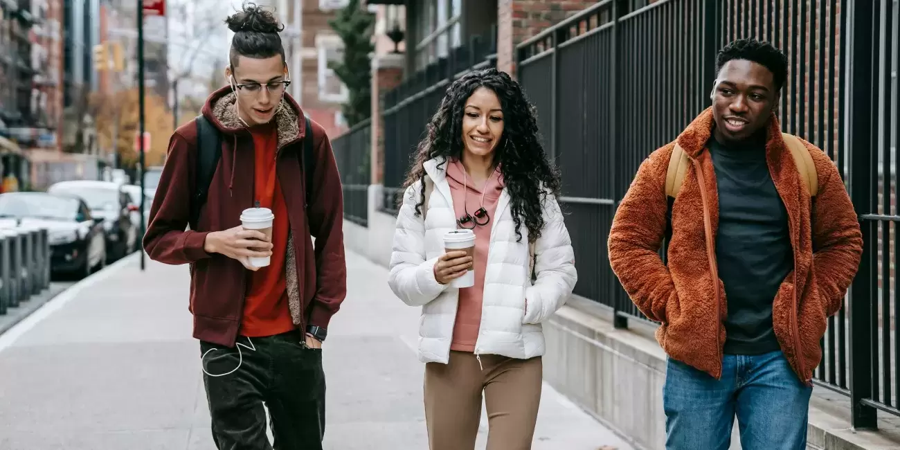 3 people in coats carrying coffee and walking