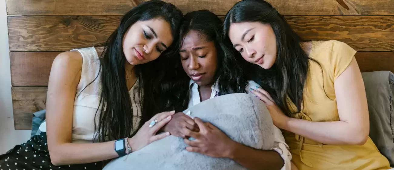 three upset people sit together comforting each other