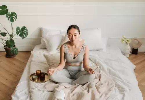 woman sits on her bed with candles next to her meditating