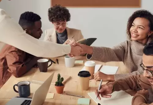 woman reaches across table of people working to shake hands with someone out of shot