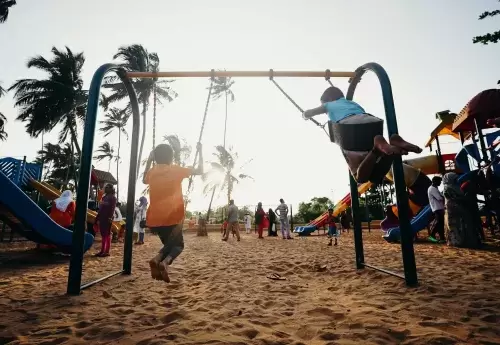 kids swinging on a playground with other people standing around