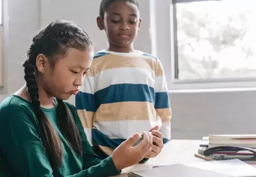 kid looks at phone and frowns while another kid looks on
