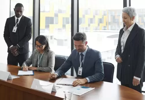 two people sit at table signing papers while two people are standing