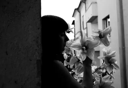 black and white picture of person standing against wall looking sad while smelling flowers