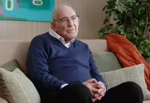 Man in blue sweater and glasses sits on couch