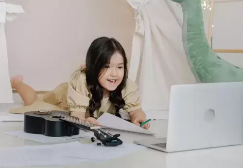 young child looks at laptop with ukelele next to them