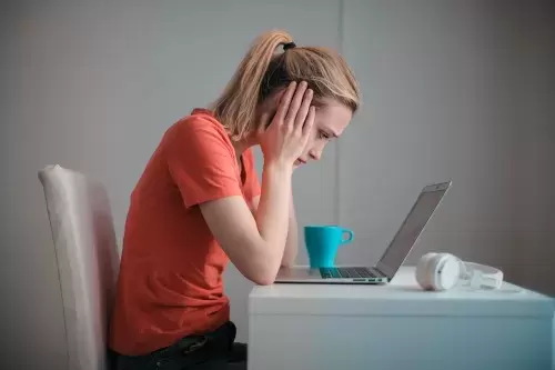 a woman hunches over her computer reading tough news with her hands on the side of her face