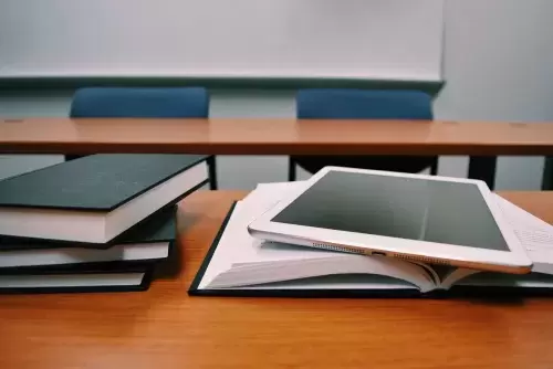 an electronic tablet rests on top of an open book on a desk next to other books