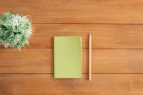 notebook and pencil on wood table next to green plant