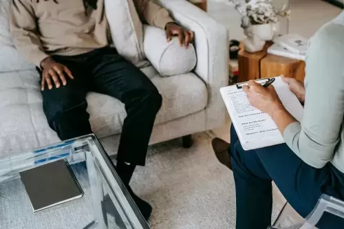 person sits on couch while another person sits across from them with clipboard and pen