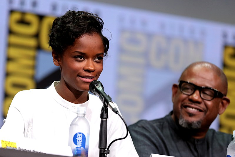 Letitia Wright is seated, speaking into a microphone; Forest Whittaker is in the background to her left