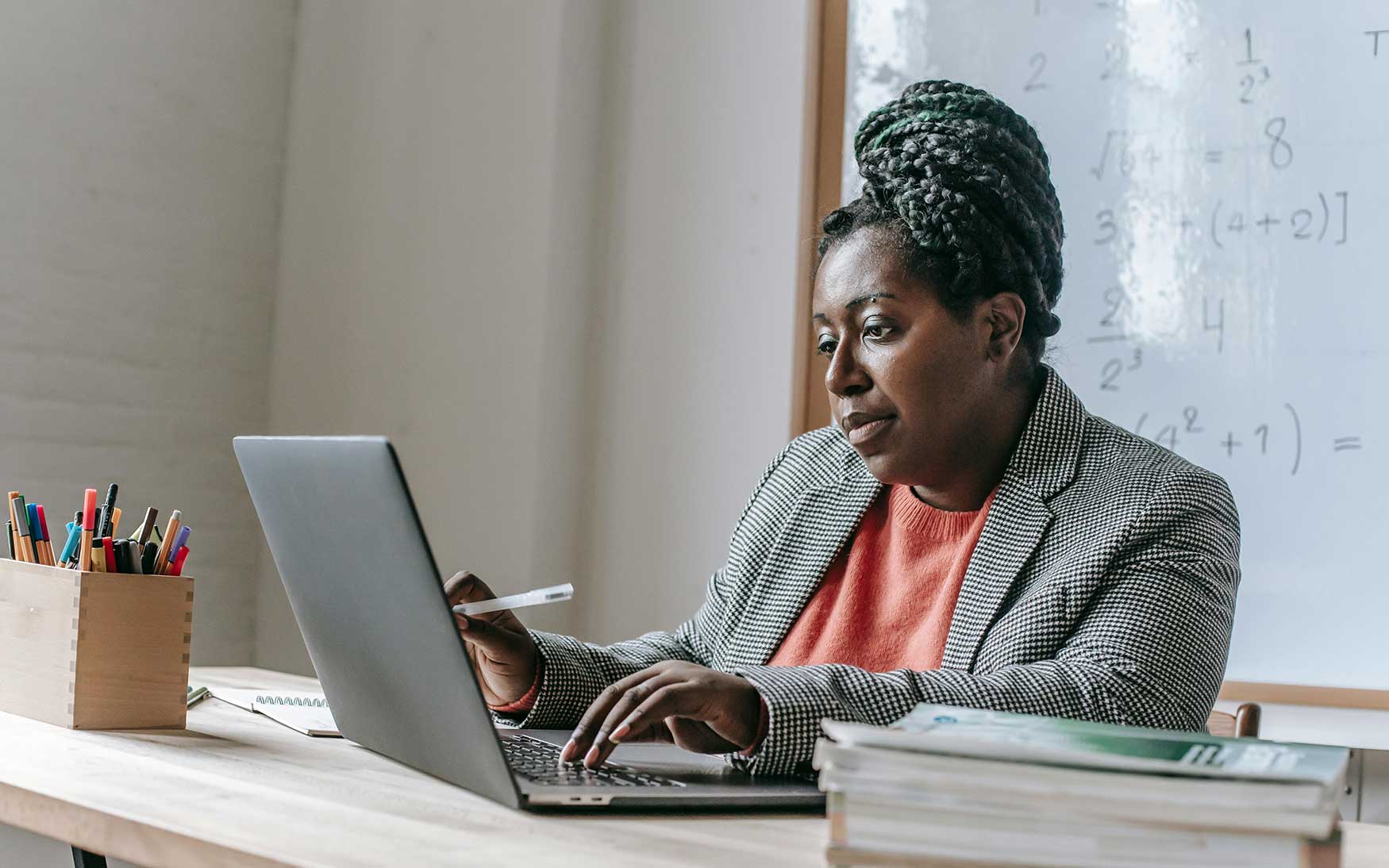 Teacher sits at desk in classroom looking at laptop