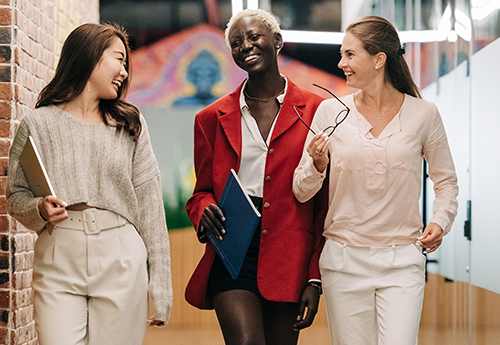 three people in business dress walk down a hallway together smiling and talking