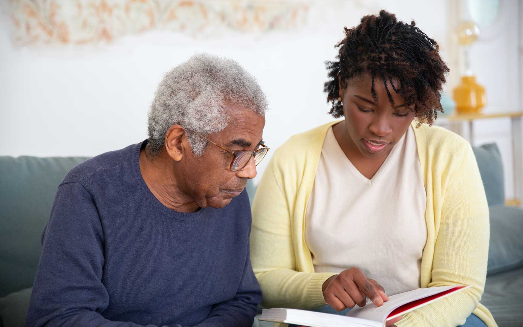 younger person helps older person looking at a book