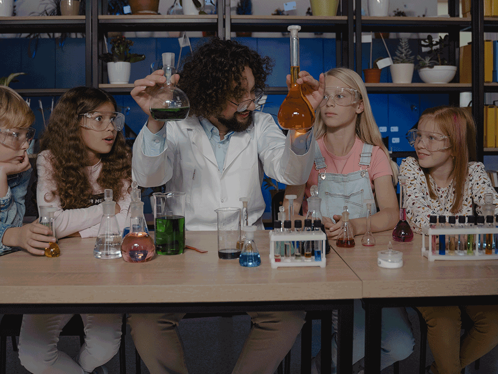 teacher holds beakers up while sitting next to 4 students