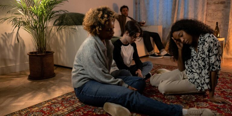 family sits in living room with two members sitting on floor comforting each other