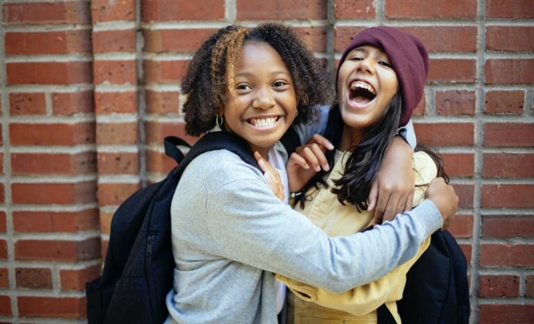 two children stand and hug each other smiling